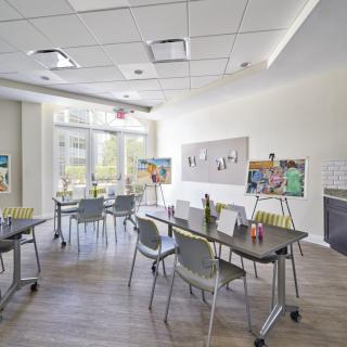 A modern classroom setup with tables and chairs arranged in a bright, open space featuring large windows and a whiteboard.