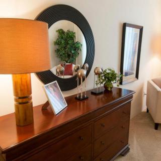 A cozy living room setup featuring a wooden sideboard with a lamp, decorative items, and a round mirror on the wall.