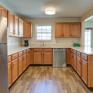 A spacious kitchen with wooden cabinets and a wooden floor, featuring modern appliances and ample natural light.