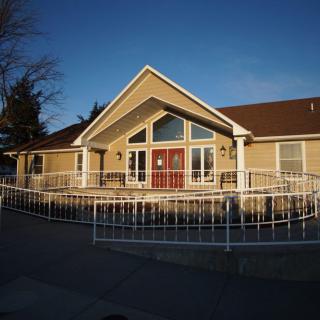 A residential house with a front yard and fence, illuminated by sunlight.