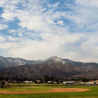 A scenic view of mountains under a partly cloudy sky, with a field in the foreground.