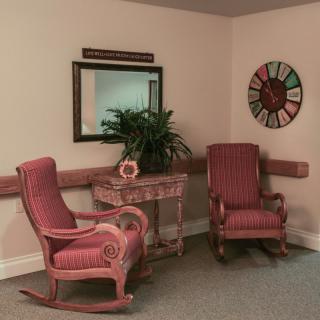 A cozy corner featuring two red rocking chairs, a decorative table with a plant, and a wall clock.