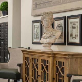 A classical bust sculpture placed on a wooden cabinet, surrounded by framed artwork in a stylish indoor setting.