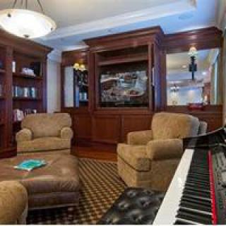 A cozy living room with a piano, surrounded by bookshelves and comfortable armchairs.