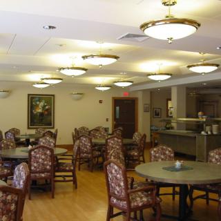 An empty dining area with patterned chairs and round tables, featuring ceiling lights and a wall painting.