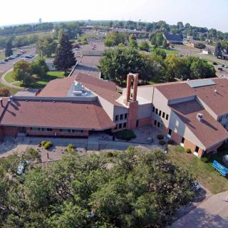 Aerial view of a church surrounded by trees with a parking lot in the background.