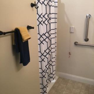 A bathroom featuring a patterned shower curtain, towel rack with towels, and a grab bar for accessibility.