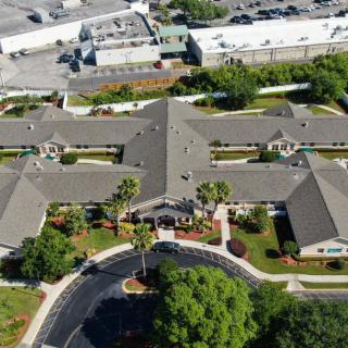 Aerial view of a large building complex surrounded by greenery and parking areas.