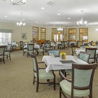 A spacious dining room with neatly arranged tables and chairs, featuring elegant lighting fixtures.