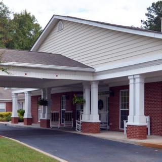 The image shows the entrance of a building with a covered porch supported by columns and a driveway leading up to it.