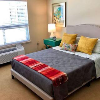 A bright and modern bedroom with a neatly made bed, colorful pillows, and a bedside lamp.
