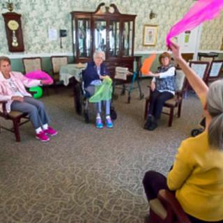 A group of seniors participating in an indoor exercise session with colorful scarves.