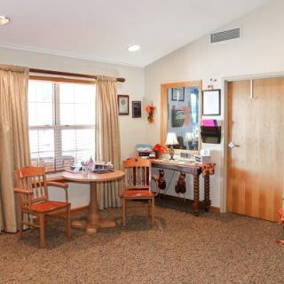A cozy living room with a small dining table and chairs by the window, adorned with simple decor and warm lighting.