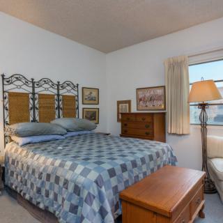 A cozy bedroom featuring a bed with a patterned quilt, artwork on the walls, and warm lighting from a standing lamp.
