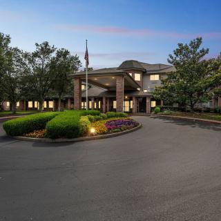 A scenic evening view of a building with a circular driveway and surrounding trees.
