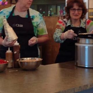 Two people wearing aprons are preparing food in a kitchen setting.