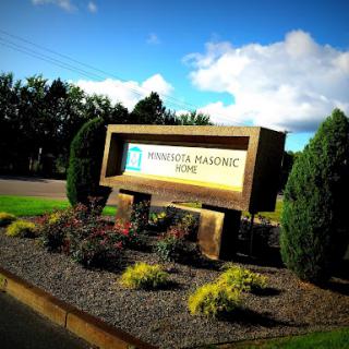 The entrance sign of a Masonic home, surrounded by well-maintained landscaping and a clear blue sky.