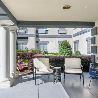 A cozy outdoor seating area on a porch with chairs and a small table, surrounded by greenery.