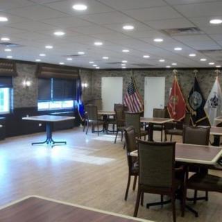 A spacious meeting room with tables and chairs, adorned with various flags and bright ceiling lighting.