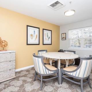 A cozy dining area with a round table surrounded by chairs, featuring artwork on the walls and a window letting in natural light.