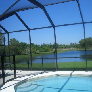 A screened-in swimming pool overlooking a scenic lake on a sunny day.