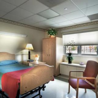 A clean and well-lit hospital room with a bed, chair, and cupboard.