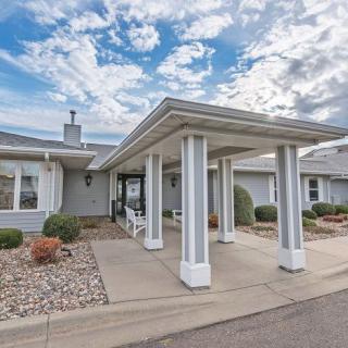 A residential building with a covered entrance and landscaped driveway under a partly cloudy sky.