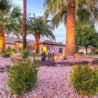 A beautiful house surrounded by palm trees and a well-maintained desert landscape at sunset.