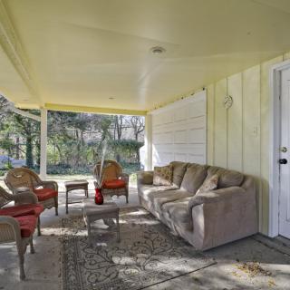 A cozy outdoor patio with comfortable seating, featuring a sofa, chairs, and a table under a covered porch.