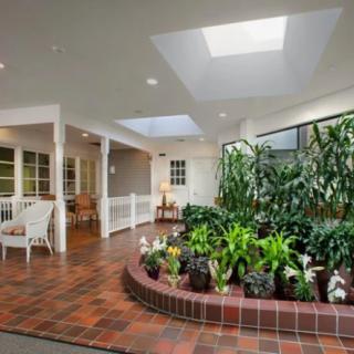 A bright indoor garden with lush plants under a skylight, complemented by a cozy seating area on brick flooring.