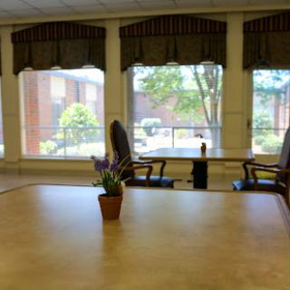 A serene interior space featuring a table and chairs, with natural light streaming in through large windows.