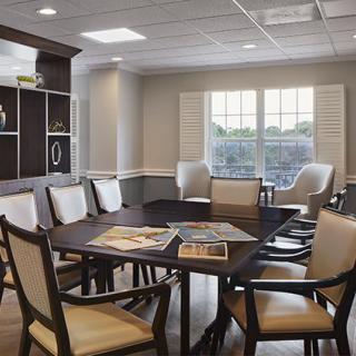 A modern meeting room with a conference table and chairs, featuring large windows and a bookshelf.