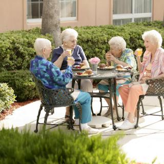 A group of elderly women enjoying a meal together outdoors on a sunny patio.