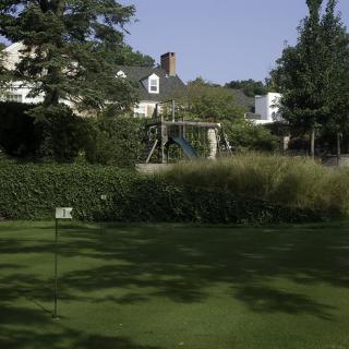 A scenic backyard with a well-maintained lawn, swing set, and a house surrounded by trees and shrubs.