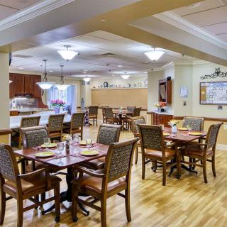A well-lit dining area with neatly arranged tables and chairs, featuring warm wooden flooring.