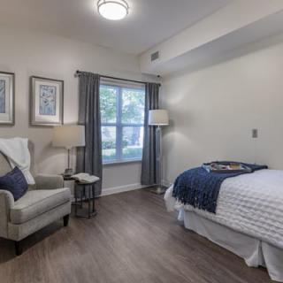 A cozy bedroom with modern decor, featuring a bed, armchair, and ample natural light.