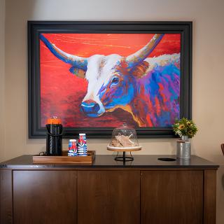 A vibrant bull painting adorns the wall above a cabinet with a coffee station and decorative elements.