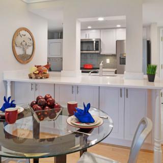 A modern kitchen and dining area featuring a glass table with red apples and blue mugs.