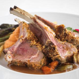 A gourmet rack of lamb served with a side of vegetables.