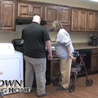 Two individuals in a care home kitchen, one using a walker while preparing food.