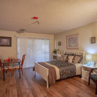 A cozy bedroom with a modern bed, small dining area, and wooden flooring.