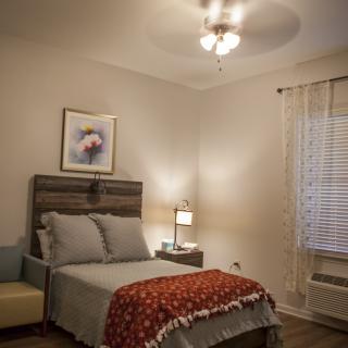 A cozy bedroom with a neatly made bed, a bedside lamp, and artwork on the wall.