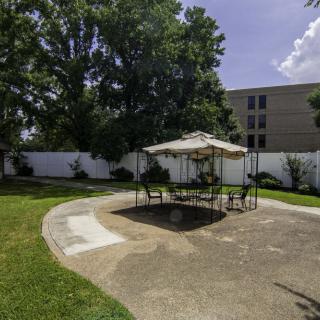 A sunny outdoor patio area with a table and umbrella surrounded by a garden and trees.