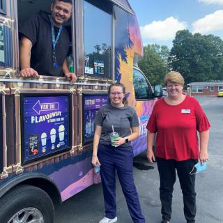 Three people, two standing outside and one leaning out of a colorful food truck.