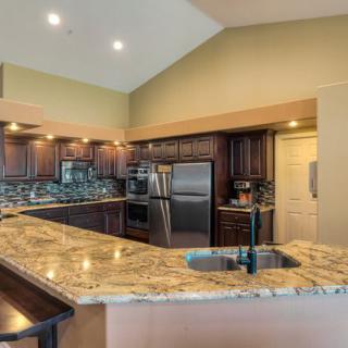 A modern kitchen featuring granite countertops, stainless steel appliances, and wood cabinets under recessed lighting.