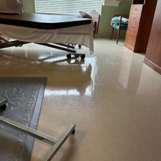 A view of a hospital room featuring a bed, furniture, and polished flooring.
