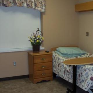 A simple hospital room with a single bed, nightstand, and flowers by the window.