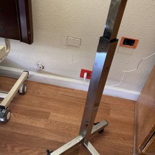A metal stand with wheels sits on a hardwood floor next to a wall outlet.