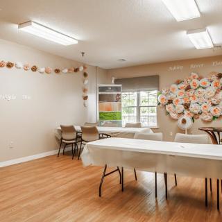 A well-lit classroom with decorated walls, tables, and chairs arranged on a hardwood floor.