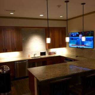 A modern kitchen with wooden cabinets, an island, pendant lighting, and a wall-mounted TV.